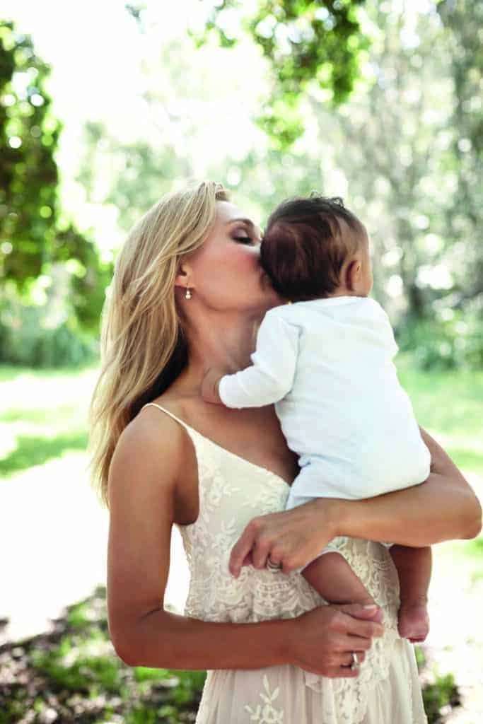 A woman affectionately kissing her baby in a park.