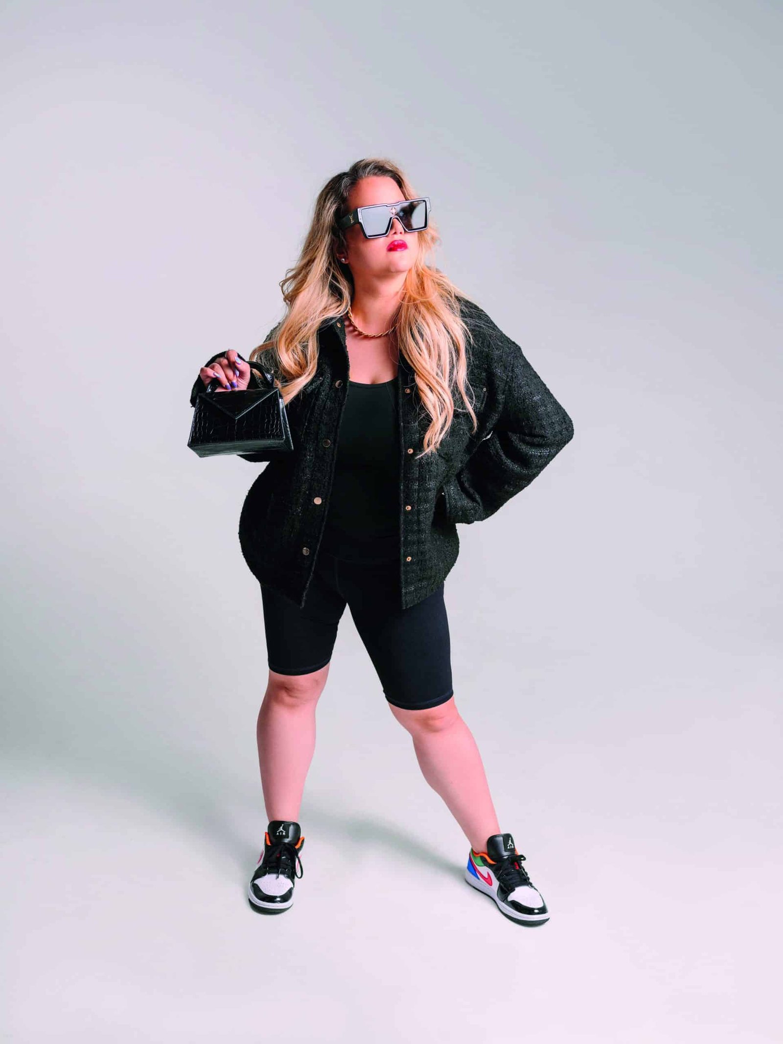 A fashion-forward woman wearing sunglasses and shorts posing on a white background.