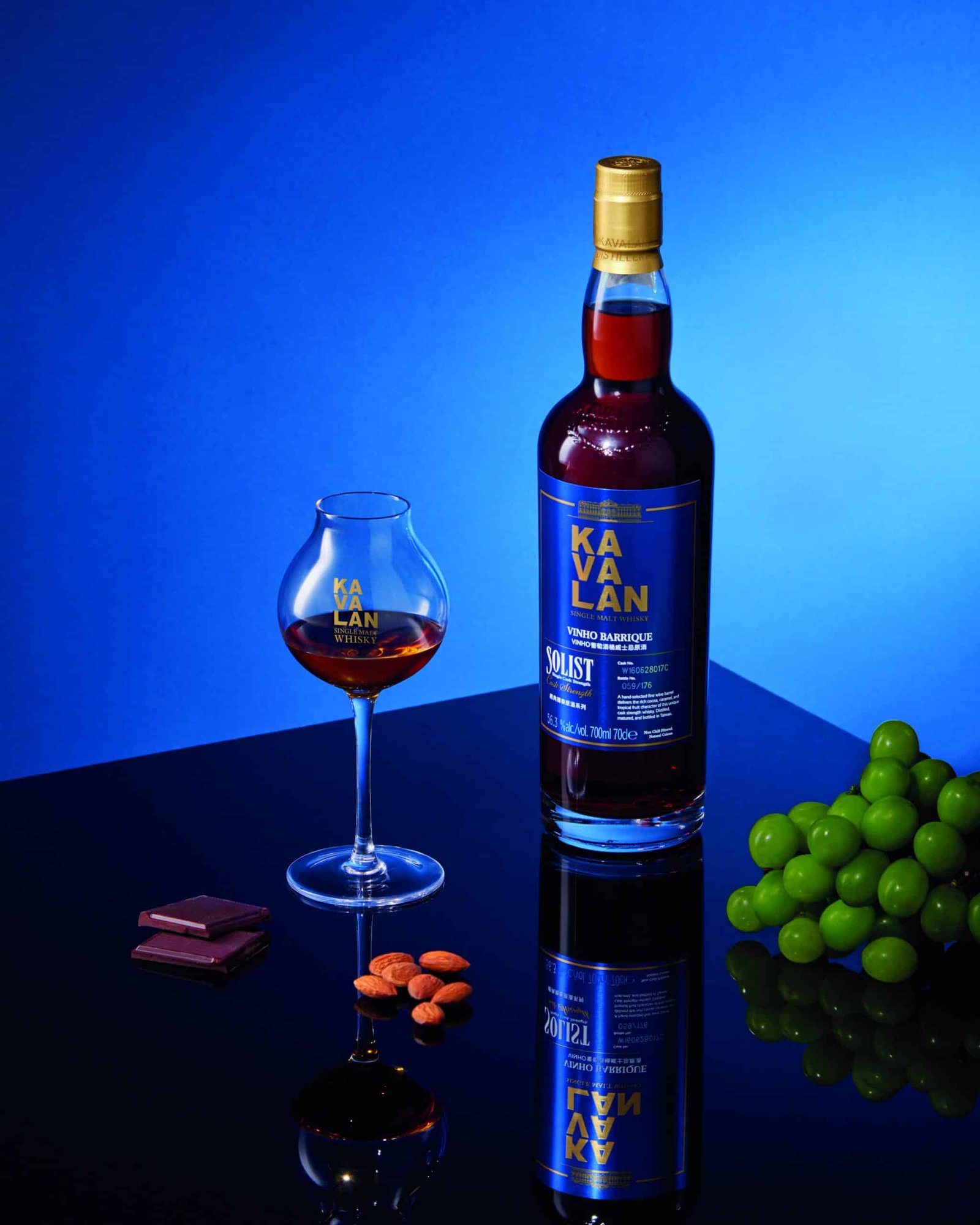 The first bottle of Taiwanese whisky and a glass of succulent grapes on a table.