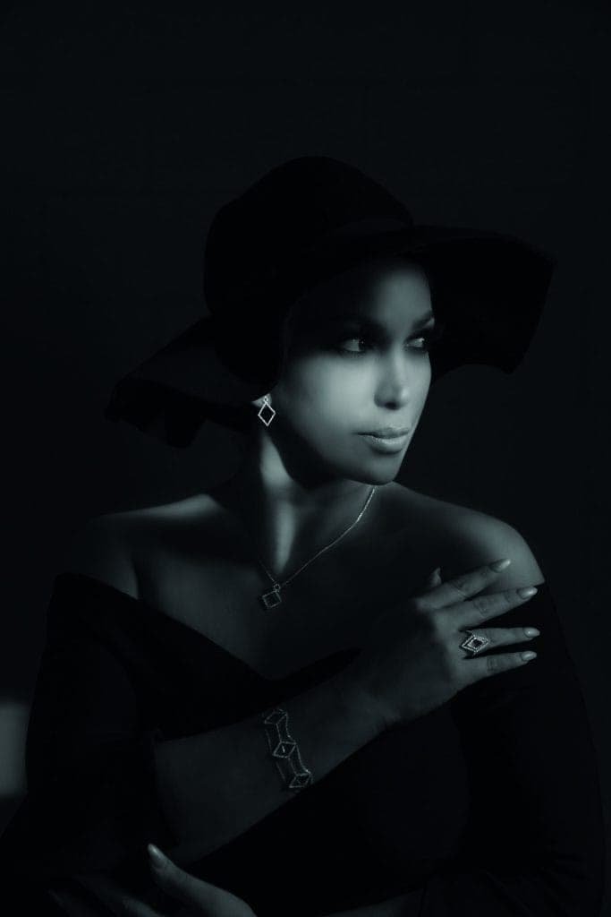A woman wearing a black hat strikes a confident pose in a dimly lit room.