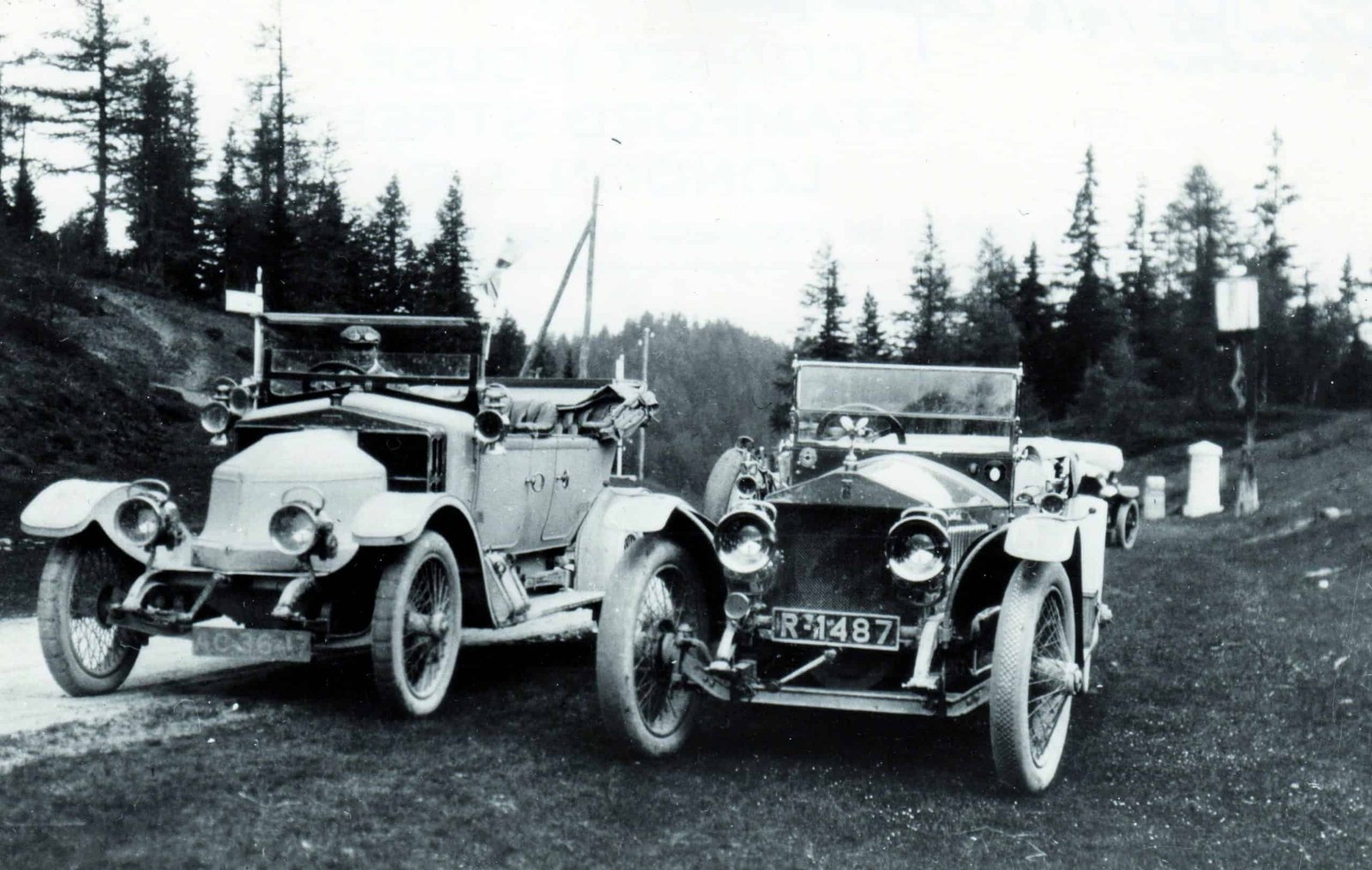 Two century-old cars parked on the side of a road.