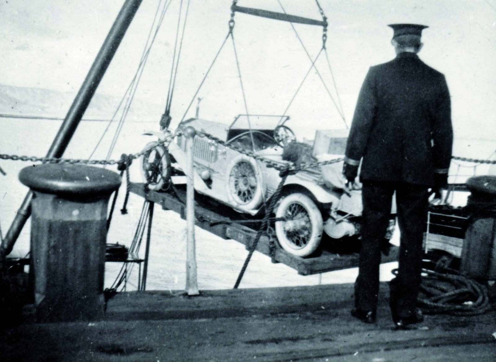 An old photo of a man lifting a car onto a boat in the early 20th century.