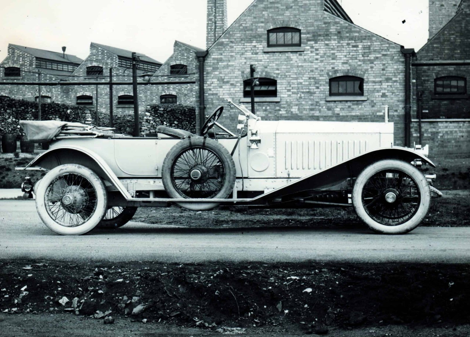 An old fashioned car parked in front of a century-old brick building.