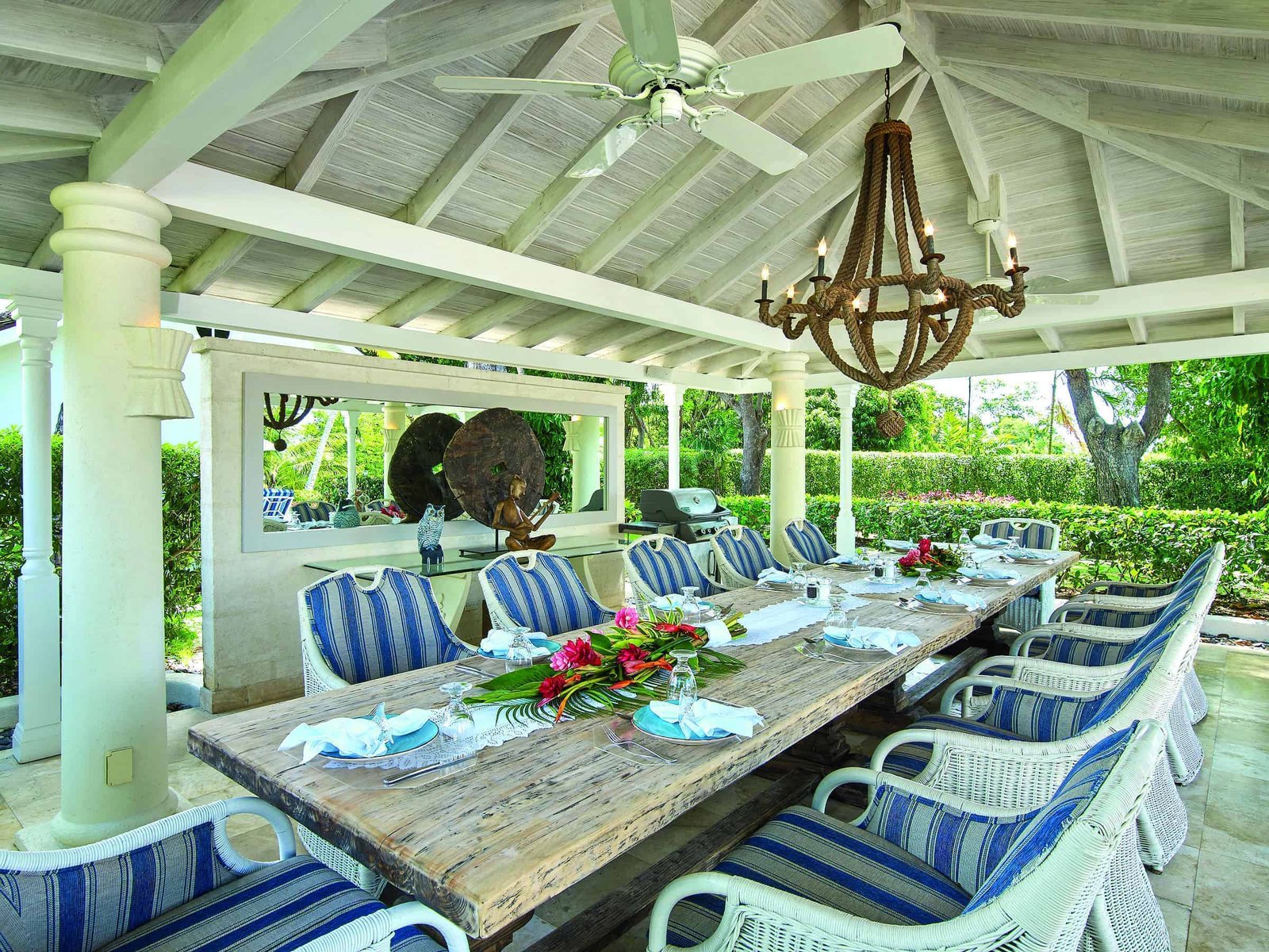 A tropical outdoor dining table with chairs and a ceiling fan, creating a paradise-like setting.