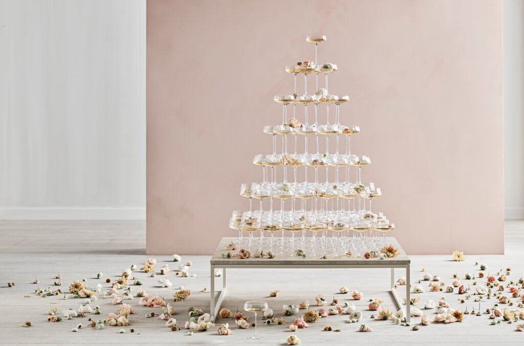 A luxury cake tower made of cupcakes on a table in front of a white wall.