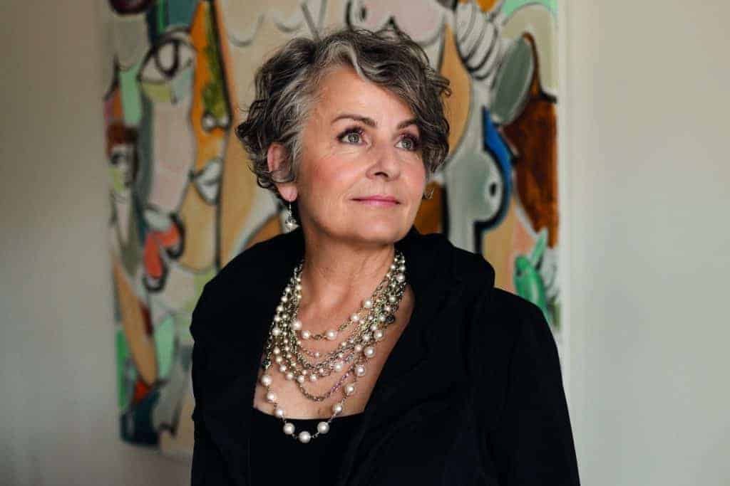 A woman in a black jacket, a statement maker, standing in front of a painting.