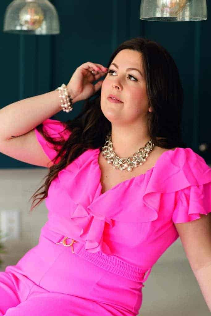 A woman in a pink jumpsuit is posing for a photo, capturing the attention as a statement maker.