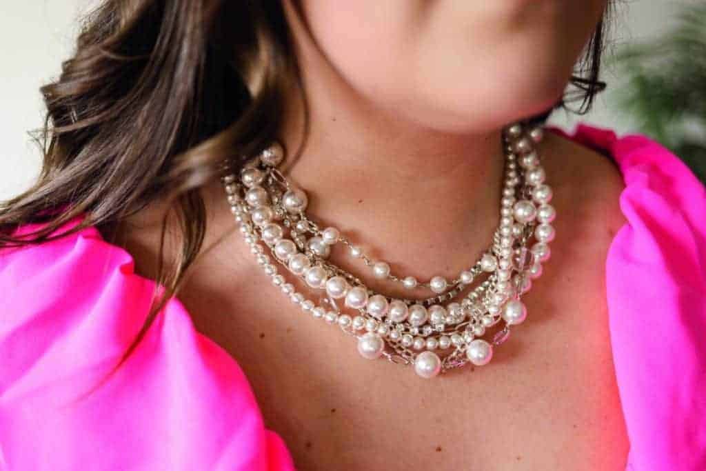 A woman wearing a pink dress and pearl necklace, giving off statement makers vibes.