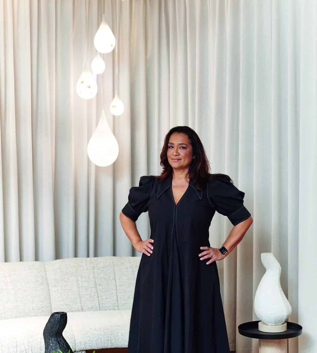 A woman in a black dress standing in front of a living room, creating a harmony between her elegant attire and the vibrant ambience.