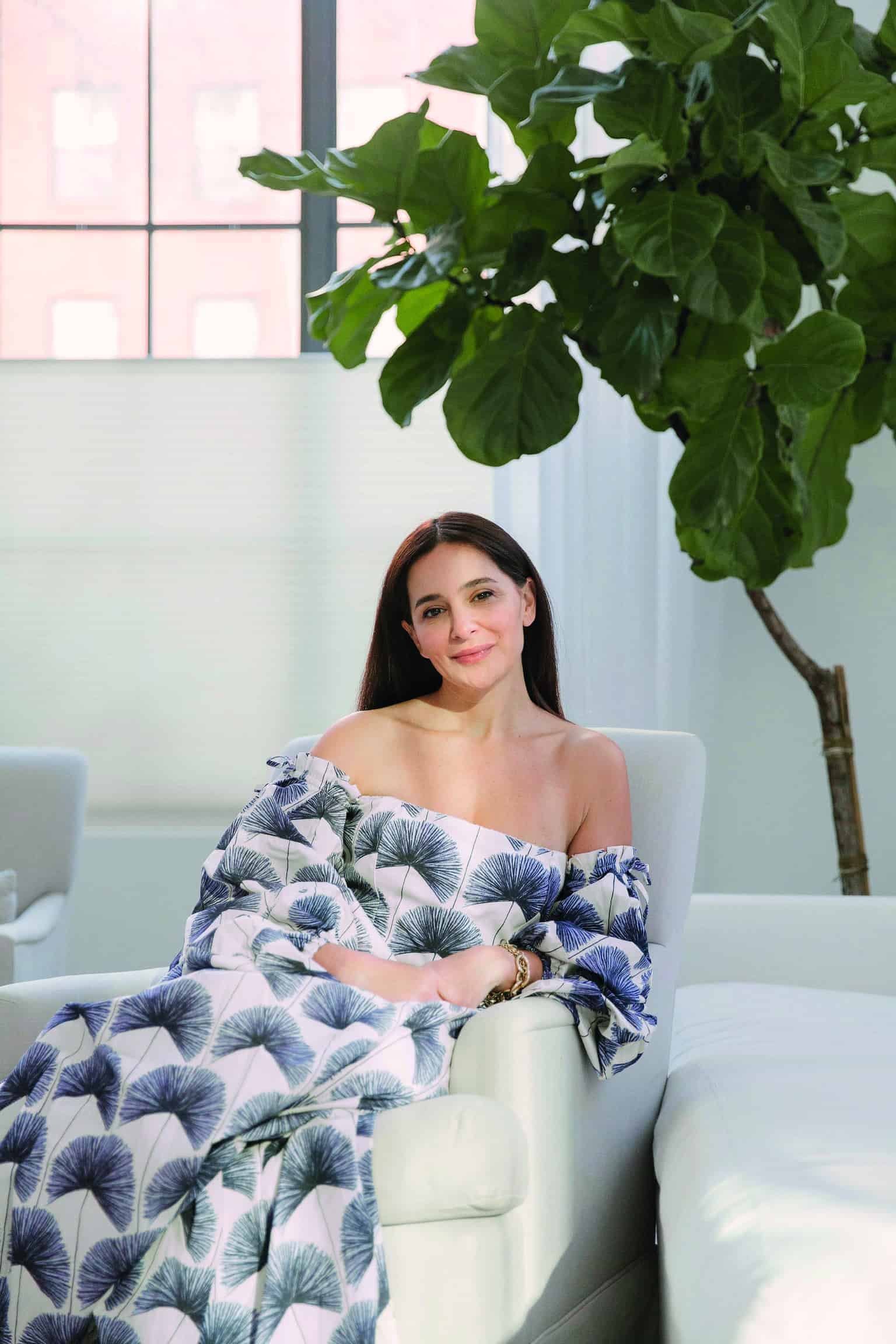 A woman in a blue and white blanket sitting in a chair next to a plant, content with what she has.