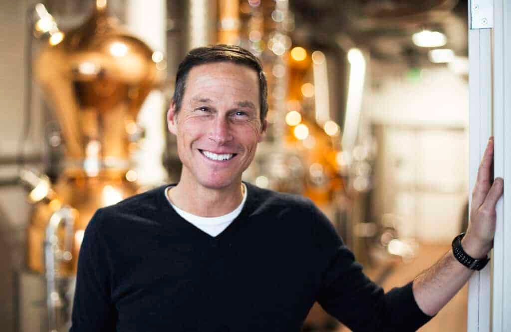 A man on a natural journey, smiling in front of a room full of bourbon barrels.