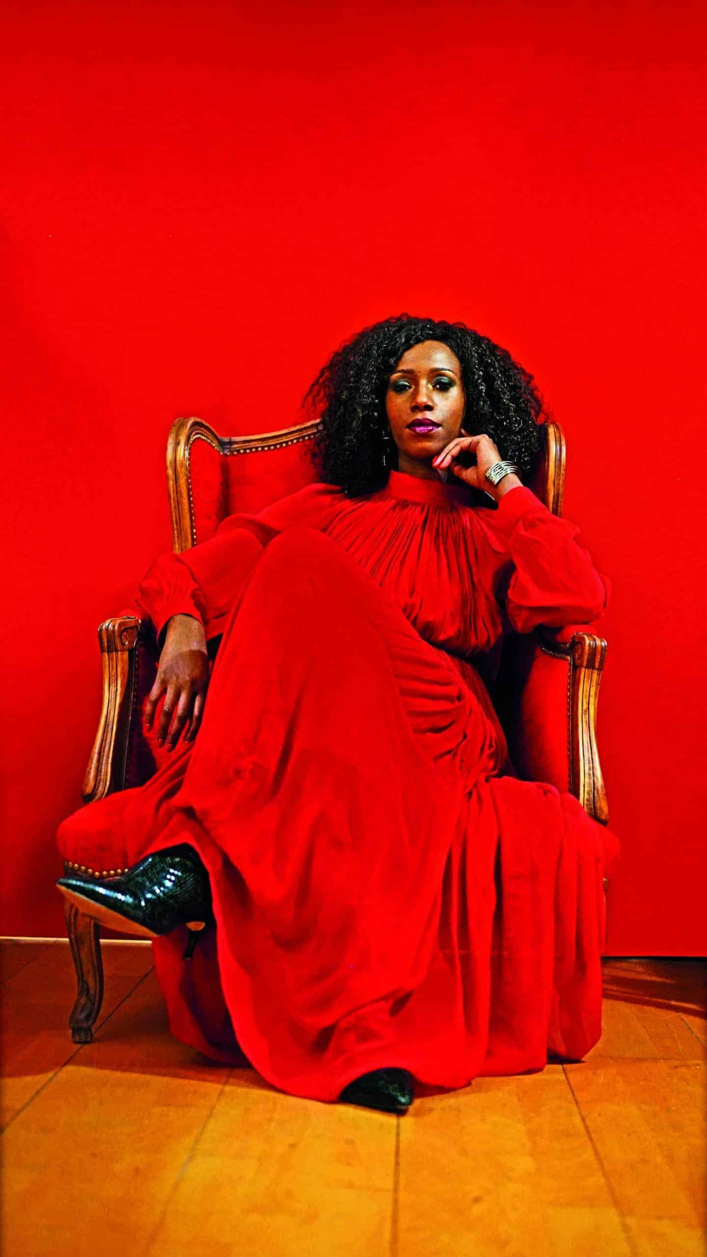 A woman with flawless skin in a red dress sitting in a chair.