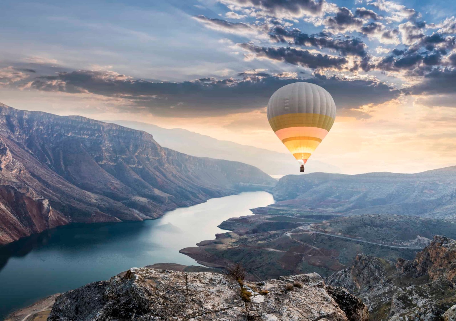 A hot air balloon is soaring over a picturesque lake, offering breathtaking travel vistas of majestic mountains.