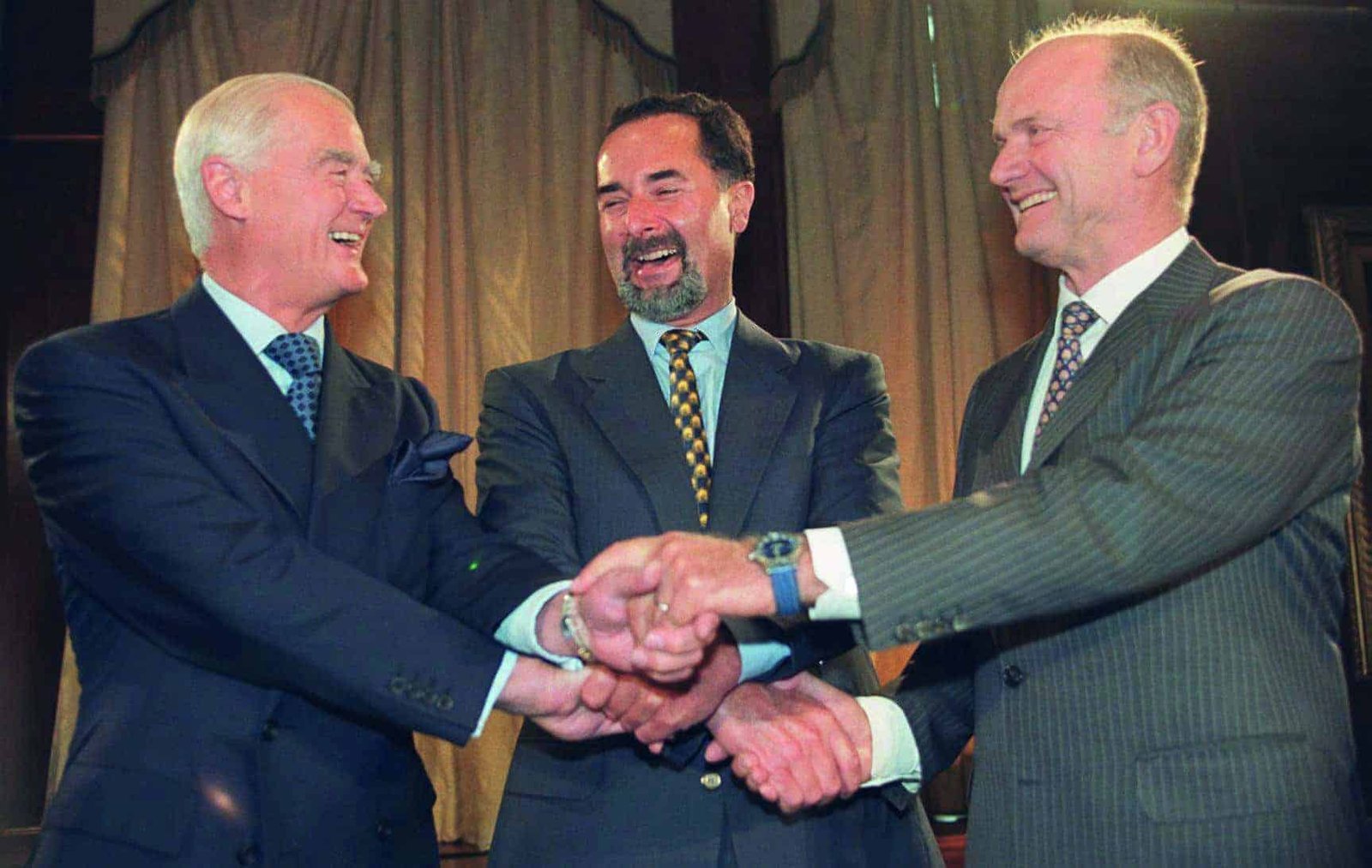 Three men in suits shaking hands with each other.