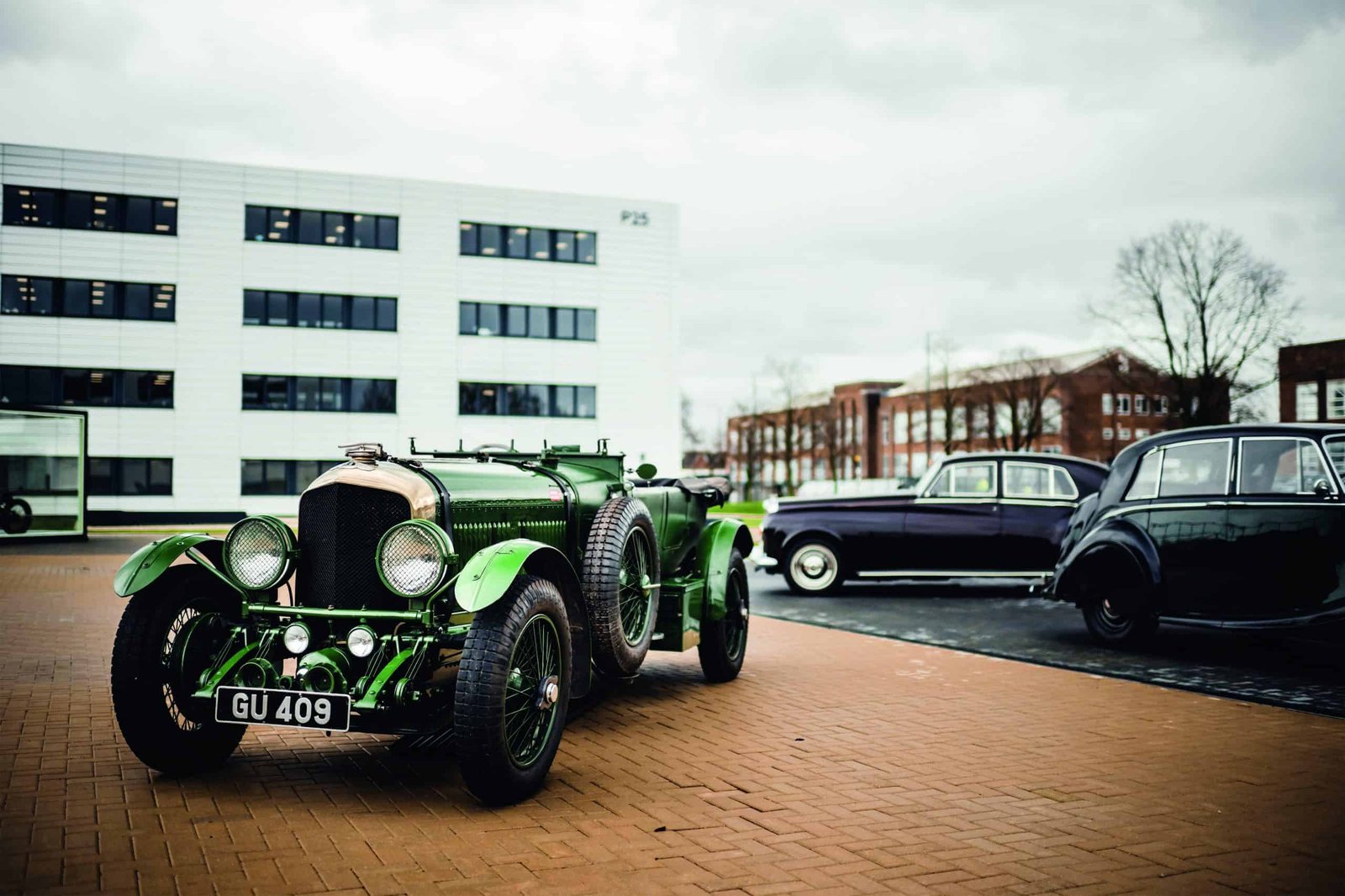 An old green car is parked in front of a building.
