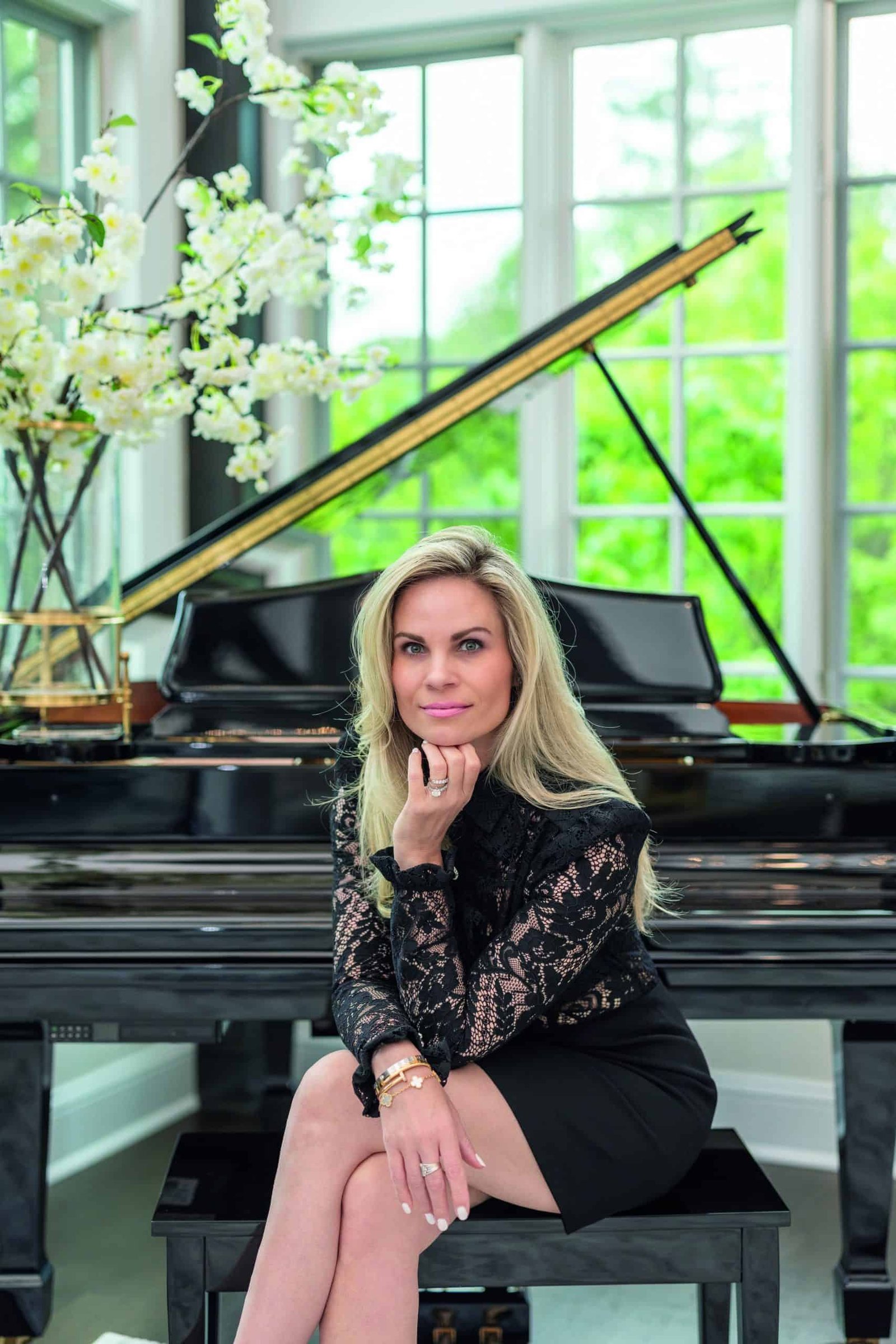 A woman in a luxurious black dress posing gracefully next to a grand piano.
