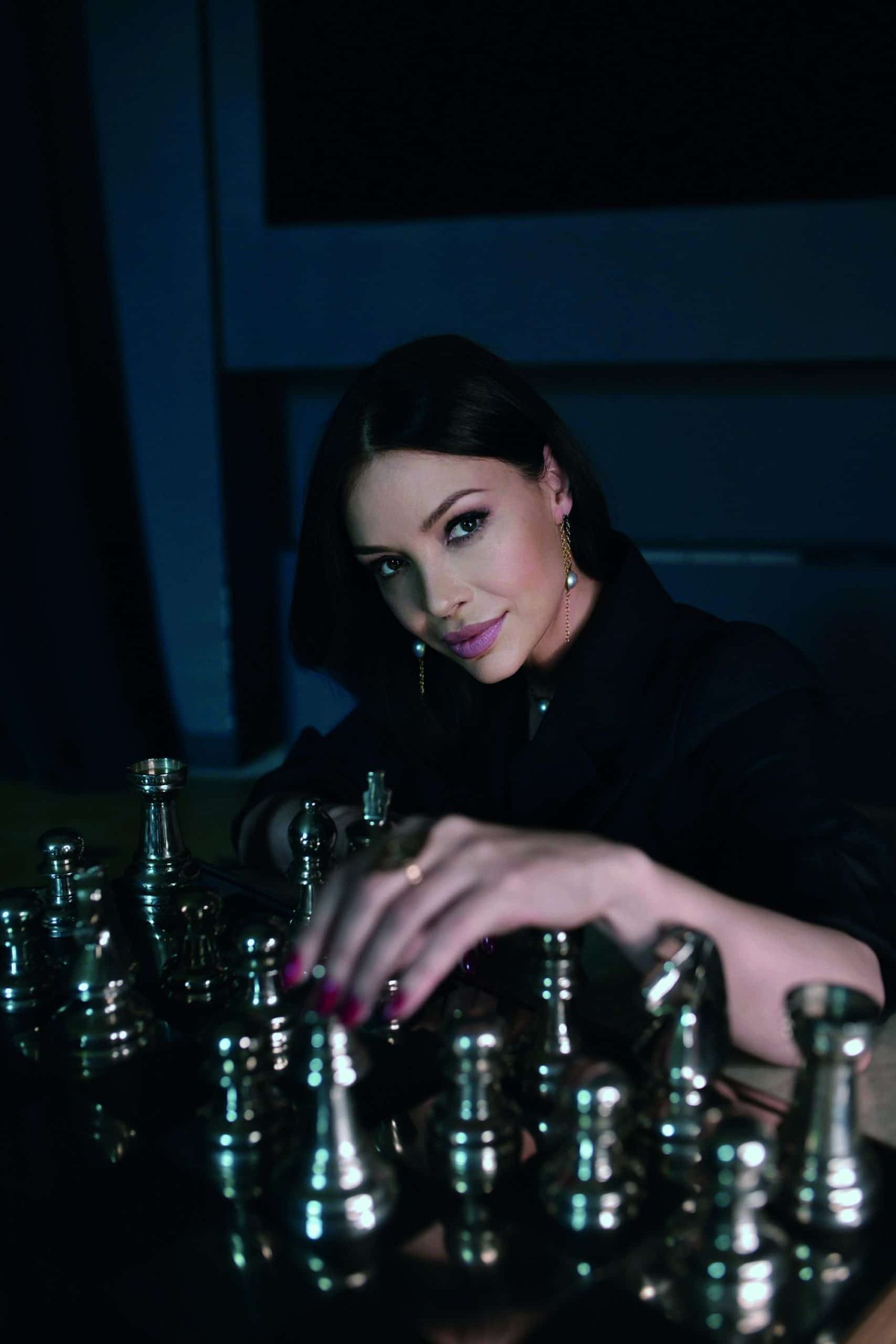 A woman playing chess in a dimly lit room, creating an atmosphere of symbolism and elegance.
