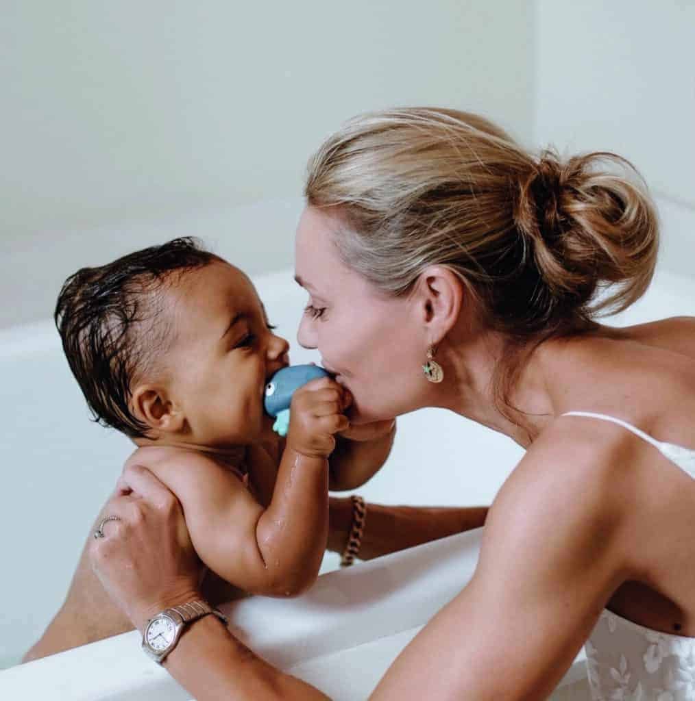 A woman carefully brushes her baby's teeth in a bathtub, ensuring every tooth is clean and healthy.