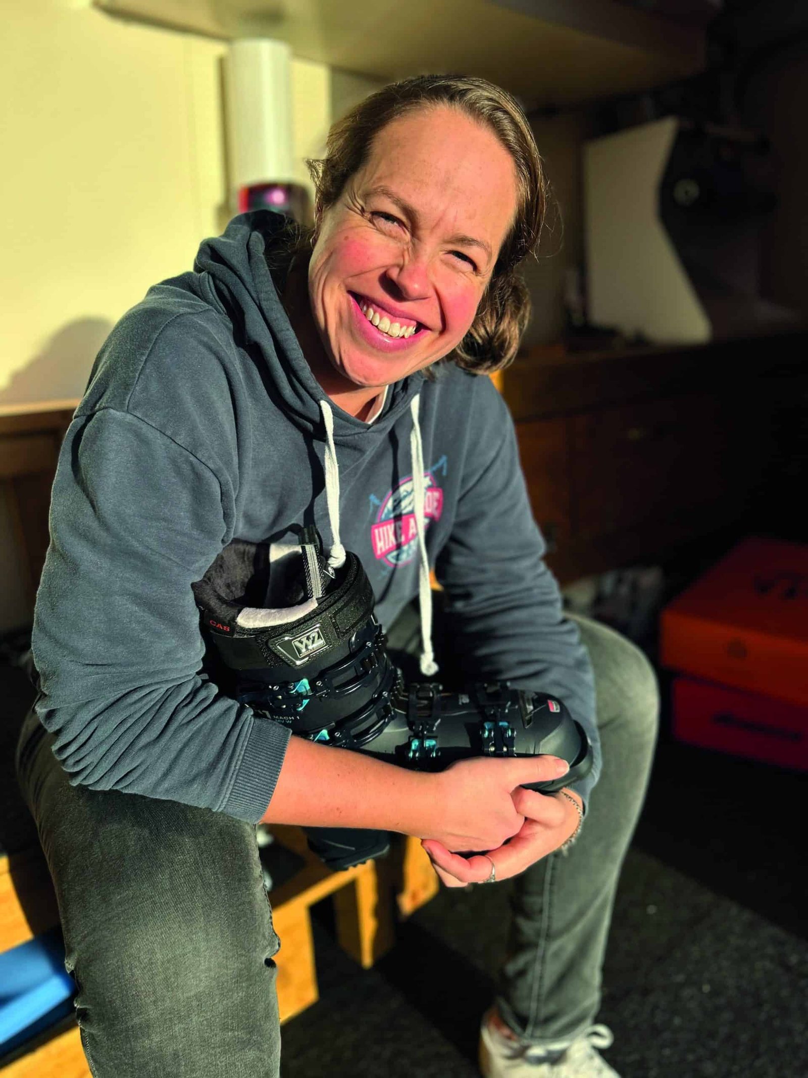 A woman wearing a hoodie and showcasing her best foot forward with a pair of ski boots.