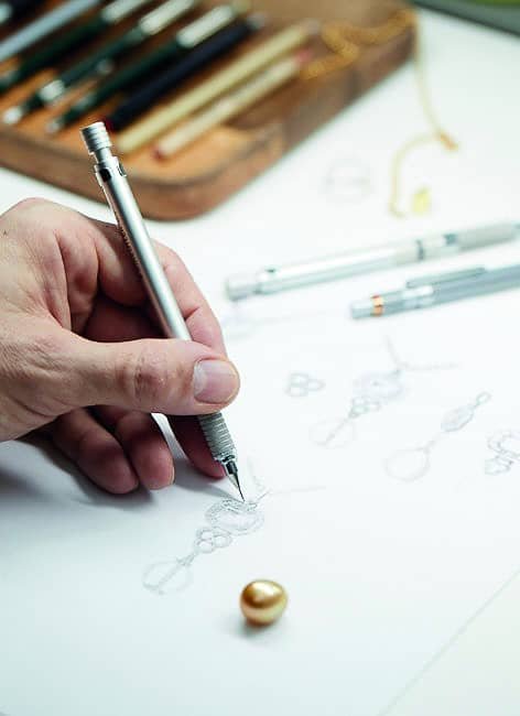 A person artistically sketching a jewel design on a piece of paper with purpose.