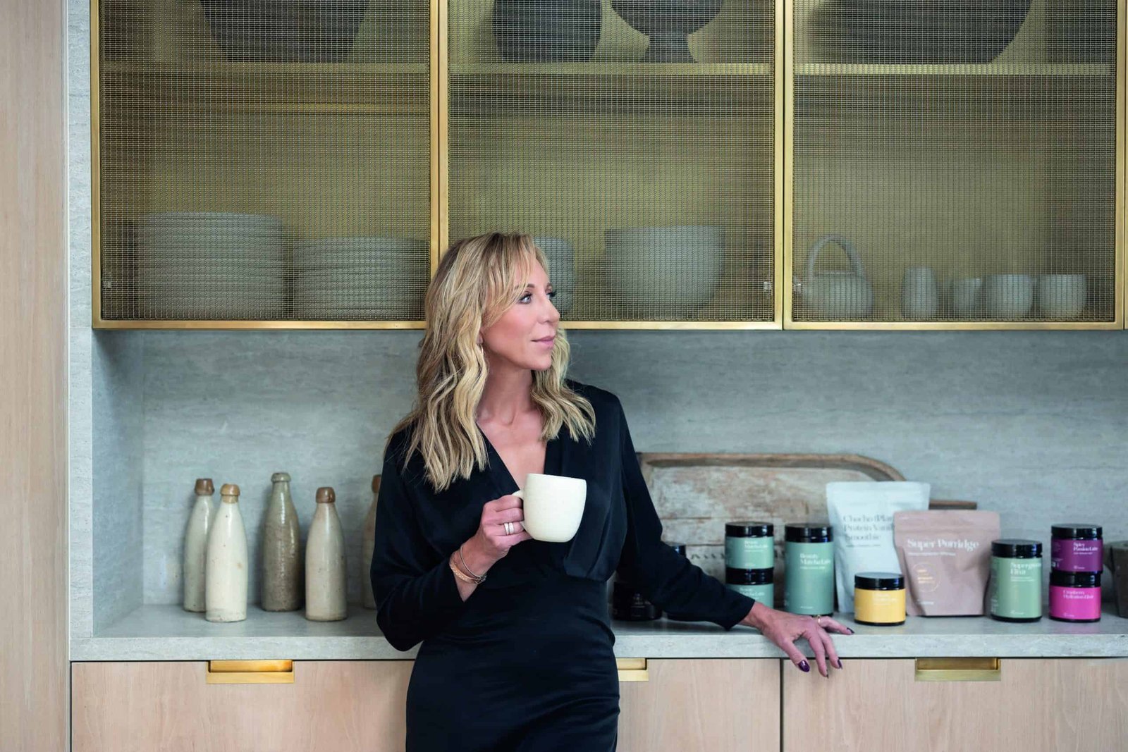 A woman in a black dress wonders in front of a kitchen.