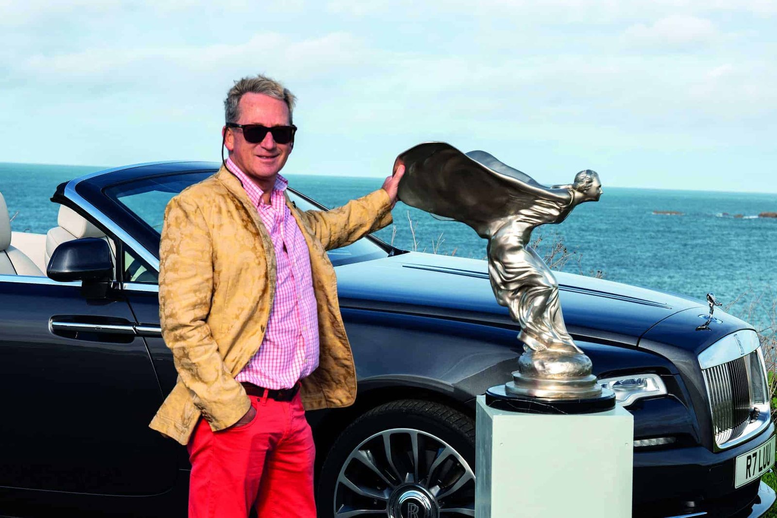 A man admiring the lasting beauty of a Rolls Royce parked next to the ocean.