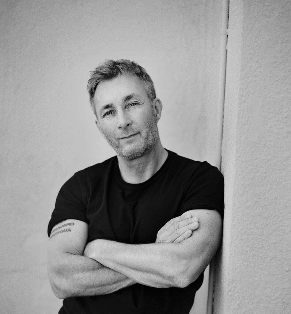 A black and white photo of a man leaning against a Scandinavian wall.