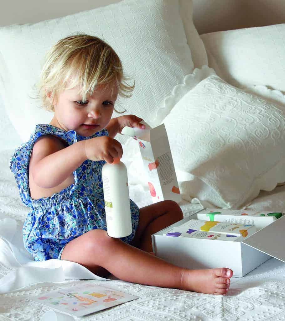 A little girl, the crème de la crème of her family, joyfully playing with a bottle on a bed.