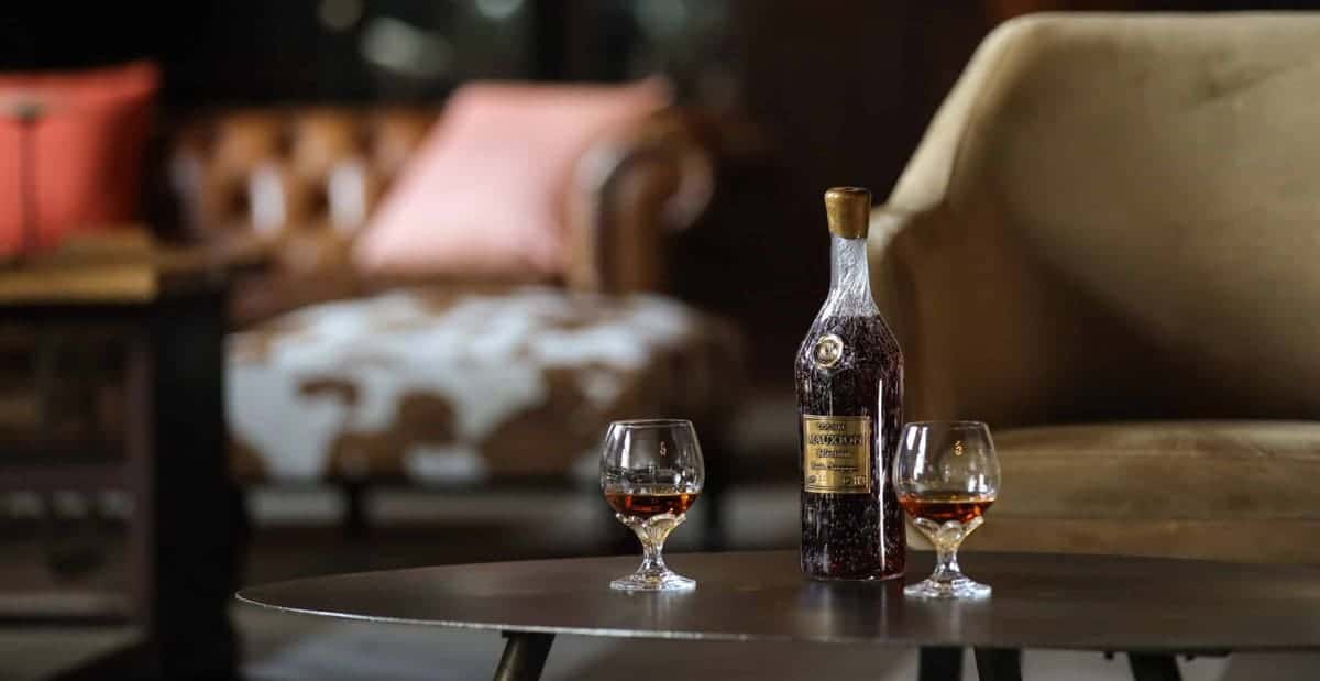 A bottle of fine whisky sits on a table next to two glasses.