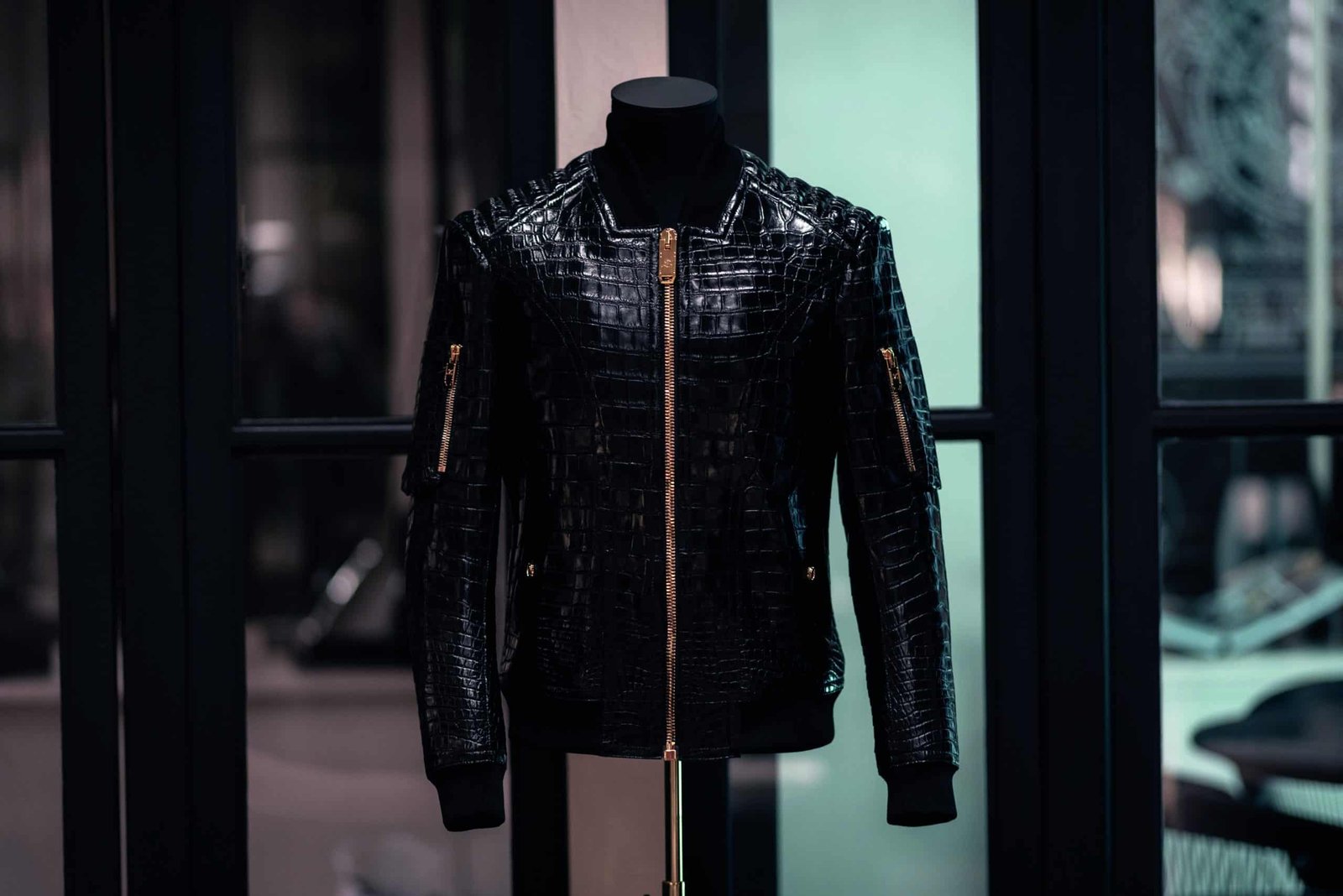 A black crocodile leather jacket hanging on a mannequin, showcasing its unique texture and high-quality craftsmanship. Its glossy finish and distinctive pattern make it a stunning piece that stands out among other