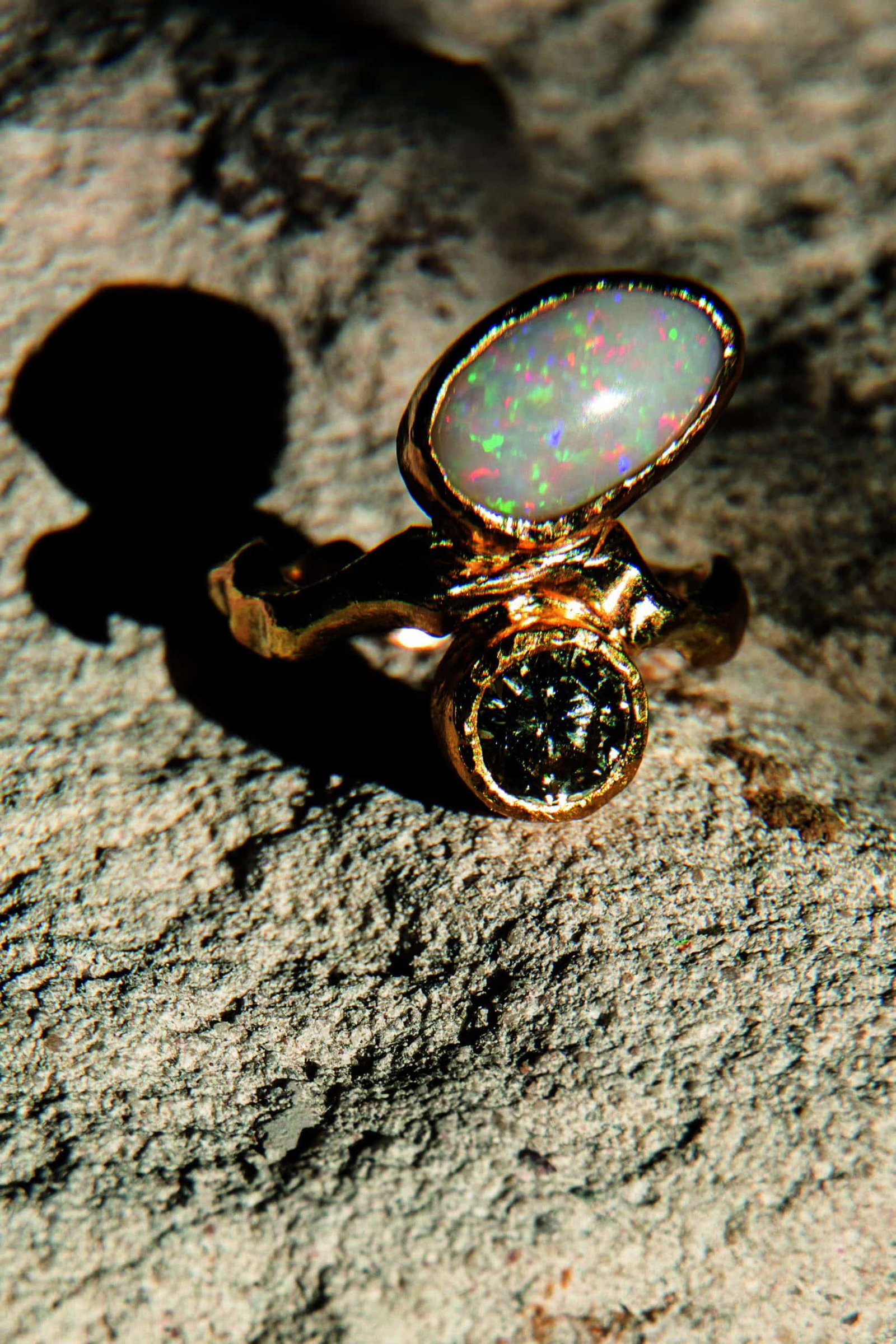 A precious opal and diamond ring sitting on a rock.
