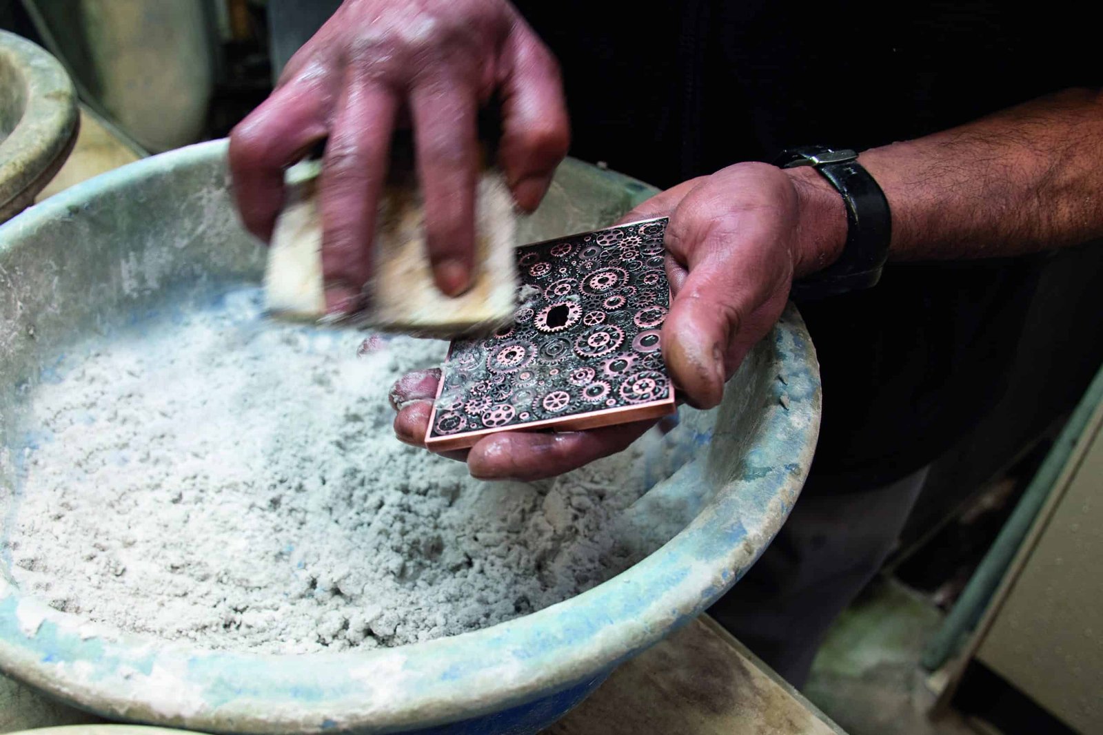 A person with impeccable style is scrubbing a piece of metal in a bowl with great savoir-faire.