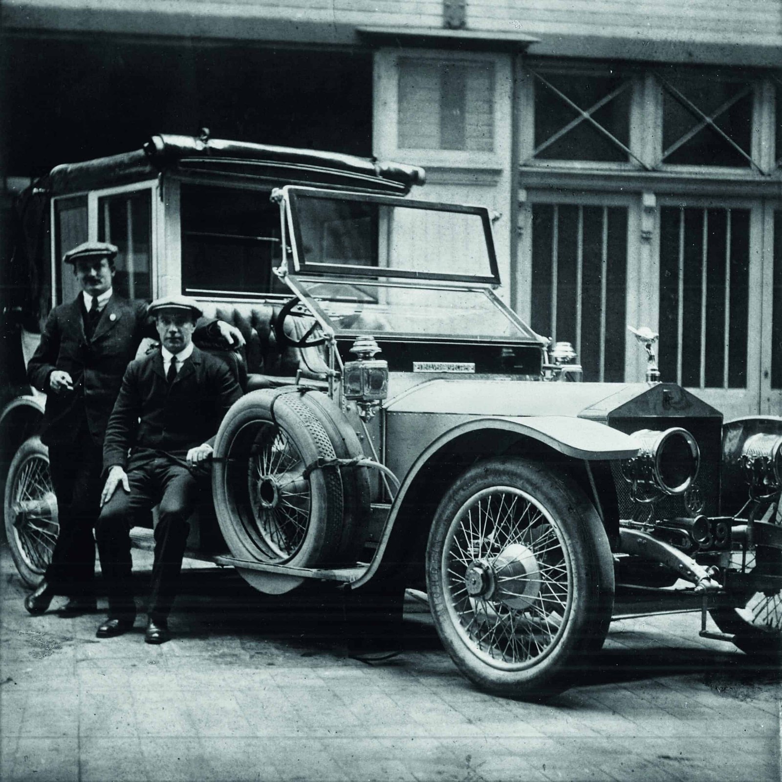 Two men standing next to a boldly designed antique car.
