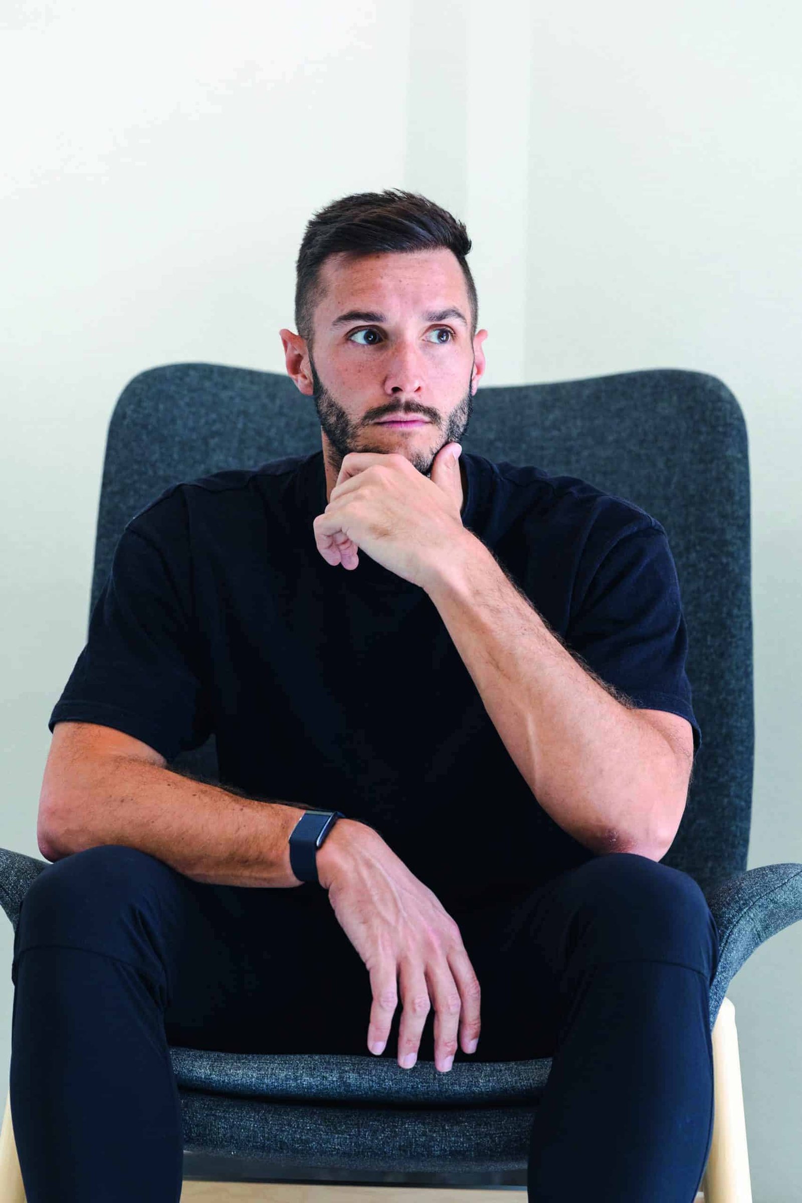 A man sitting in a chair with a contemplative expression on his face, his hand on his chin.
