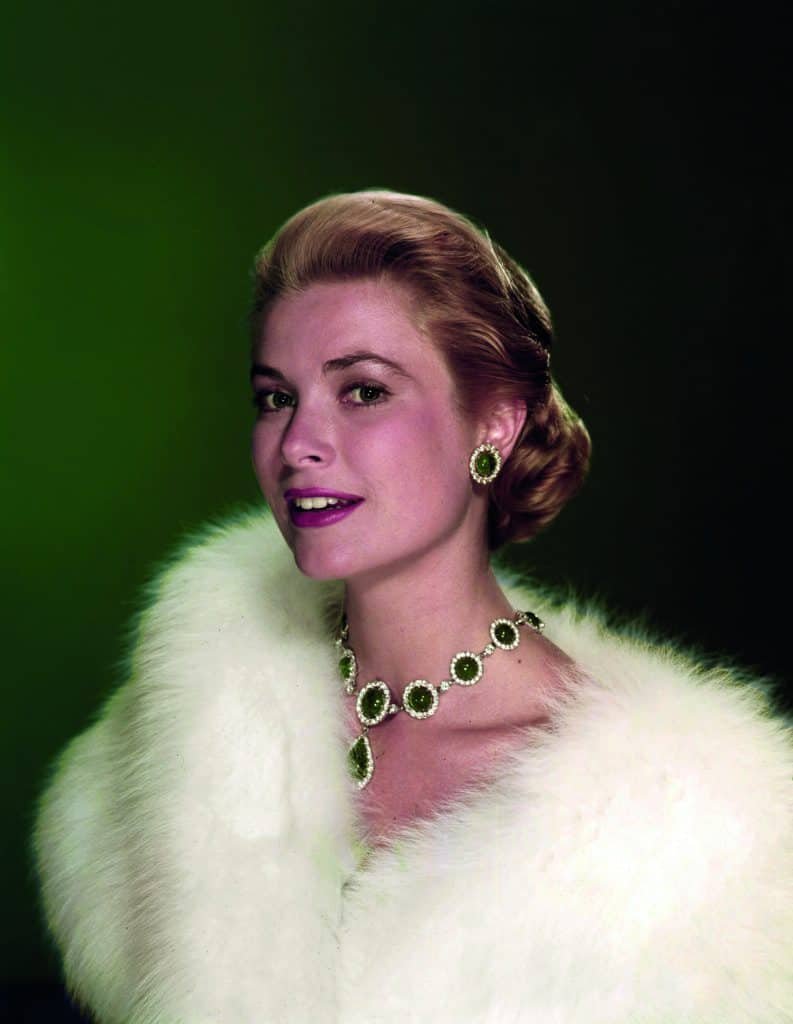 A woman in a white fur coat posing in front of a green background like a fit princess.