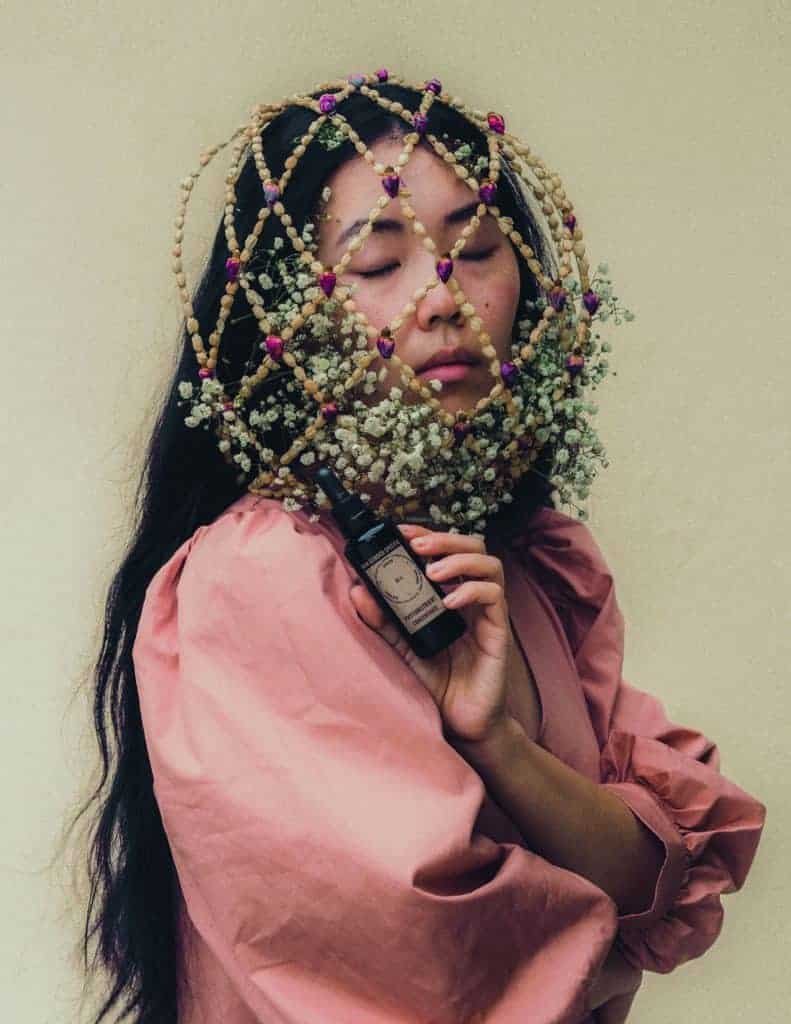 A woman wearing a flower headpiece holding a bottle of oil, radiating alluring beauty.