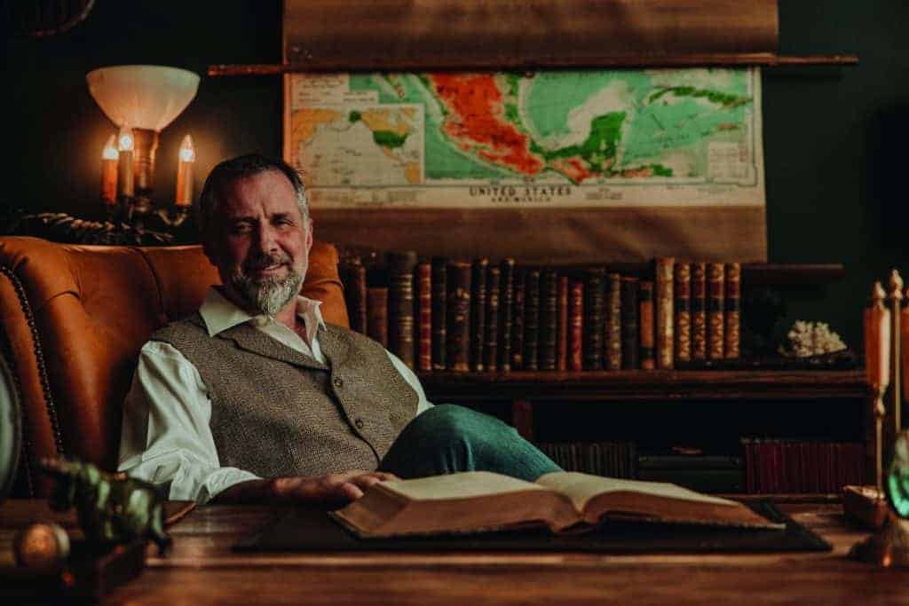 A man sitting in a chair engrossed in an open book, contemplating the lasting wisdom within its pages.