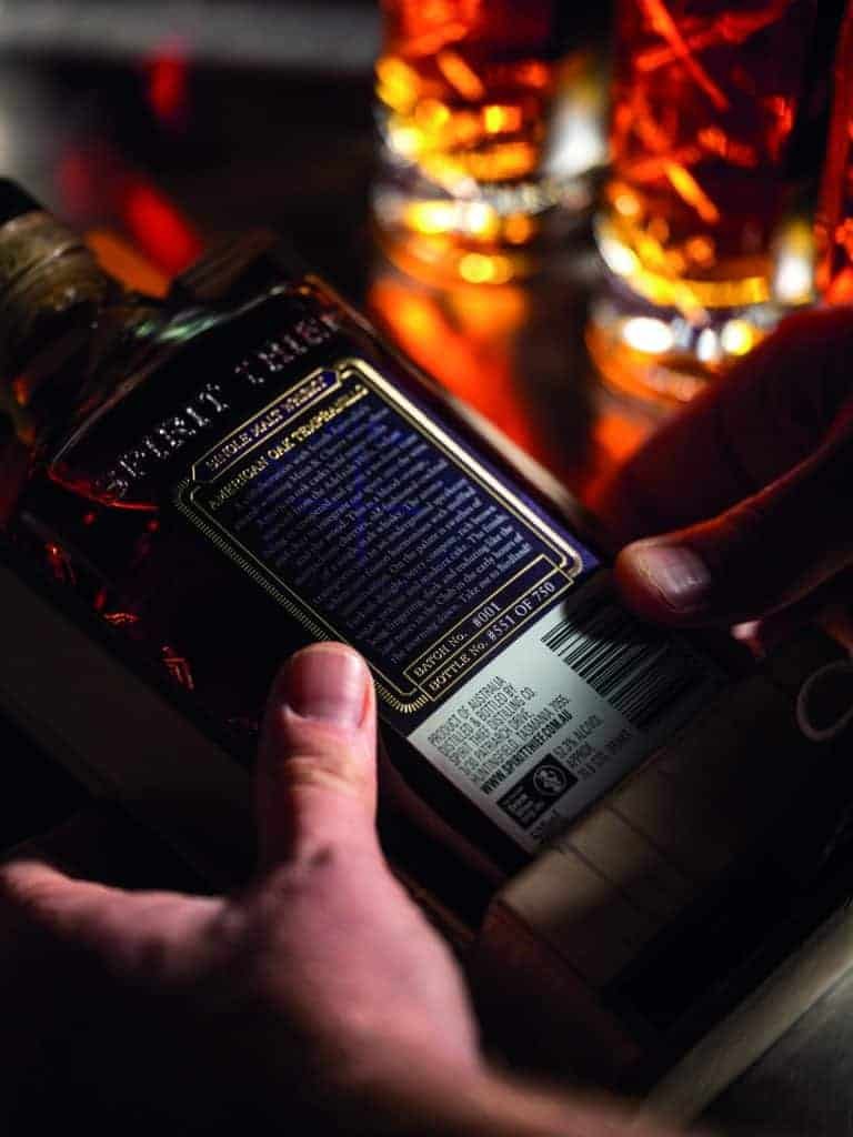 A person holding a bottle of grain whiskey.