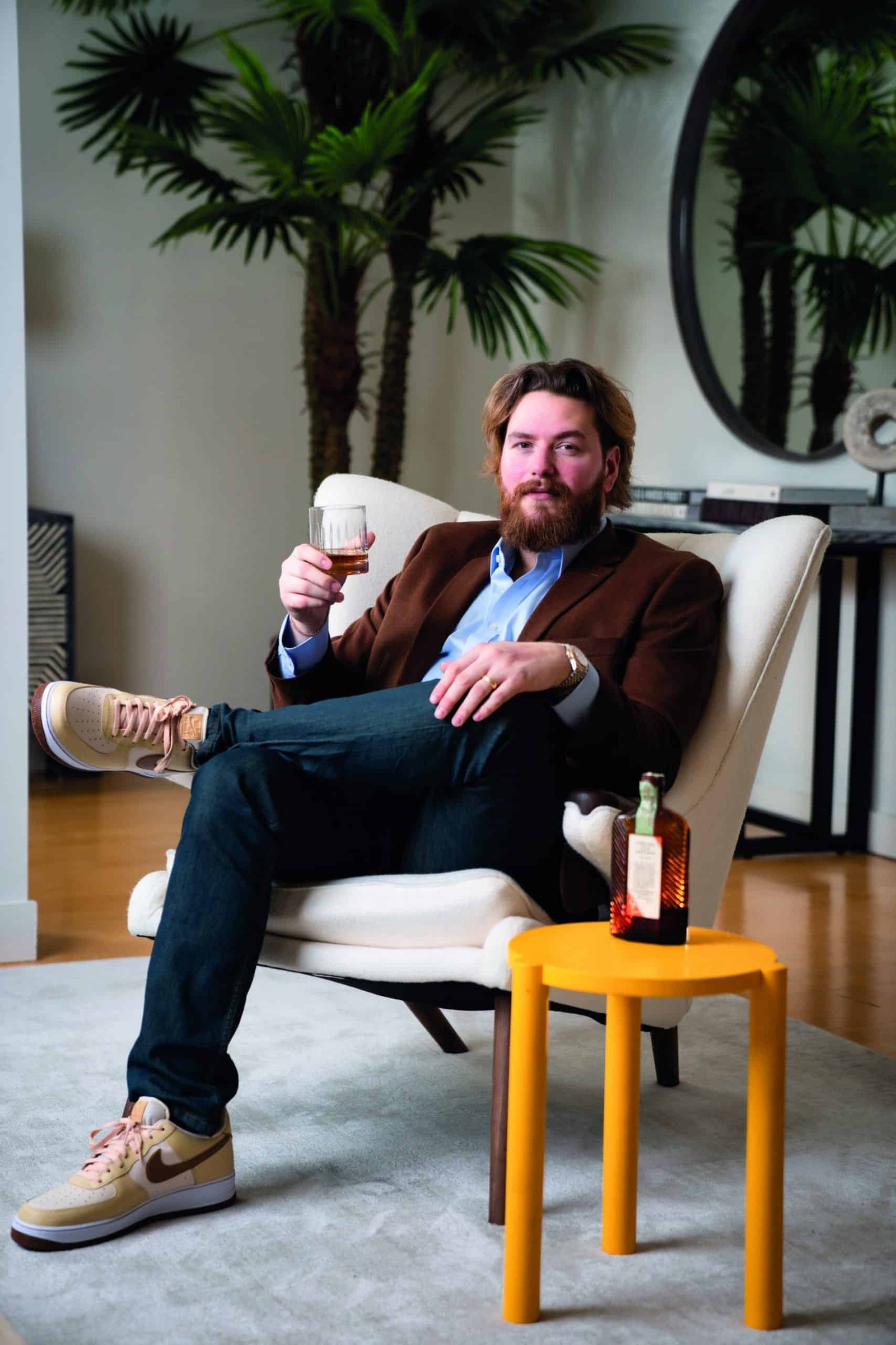 A man sitting in a chair holding a bottle of whiskey, showcasing his liquid asset.