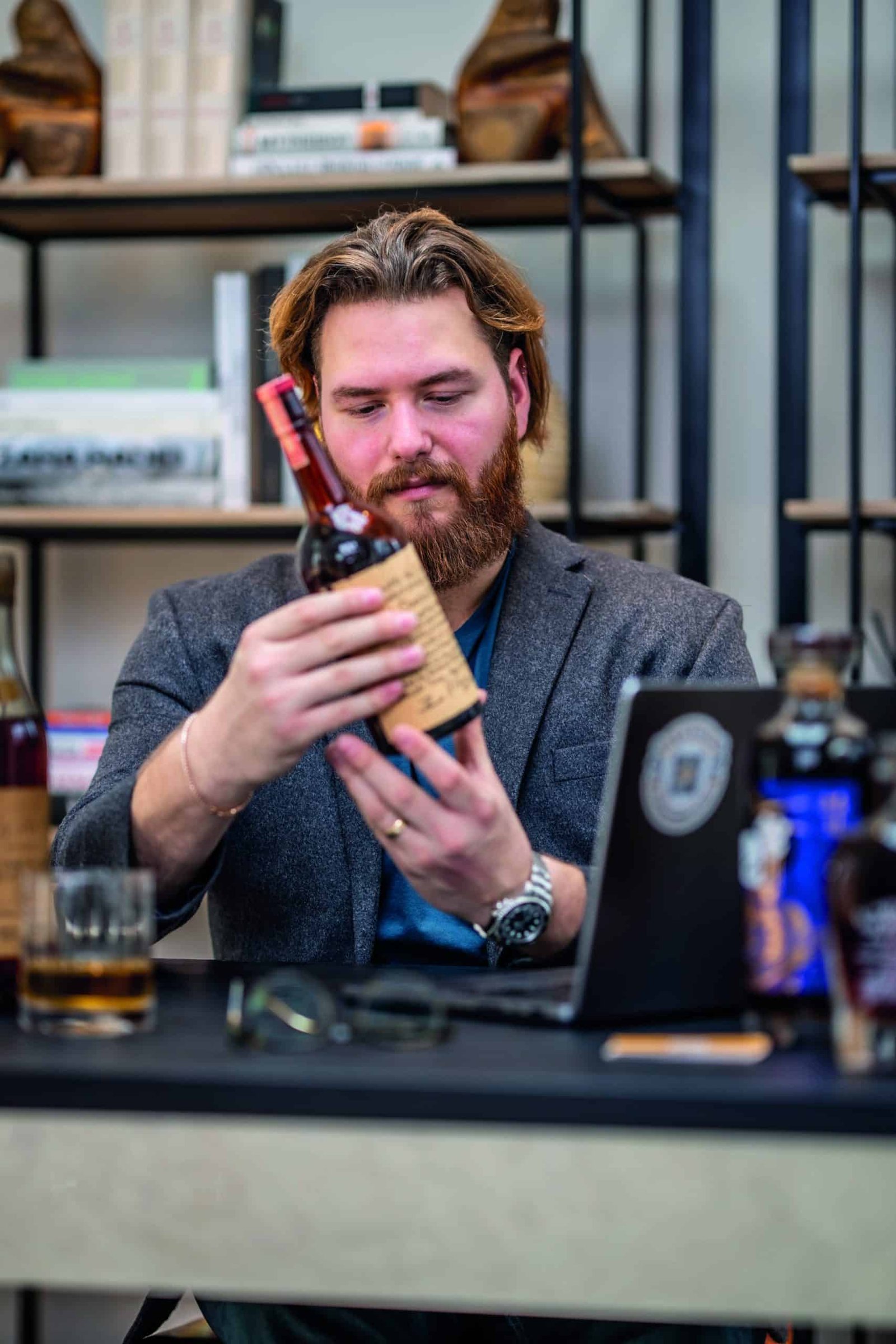 A bearded man examining a bottle of whiskey, pondering its liquid qualities.