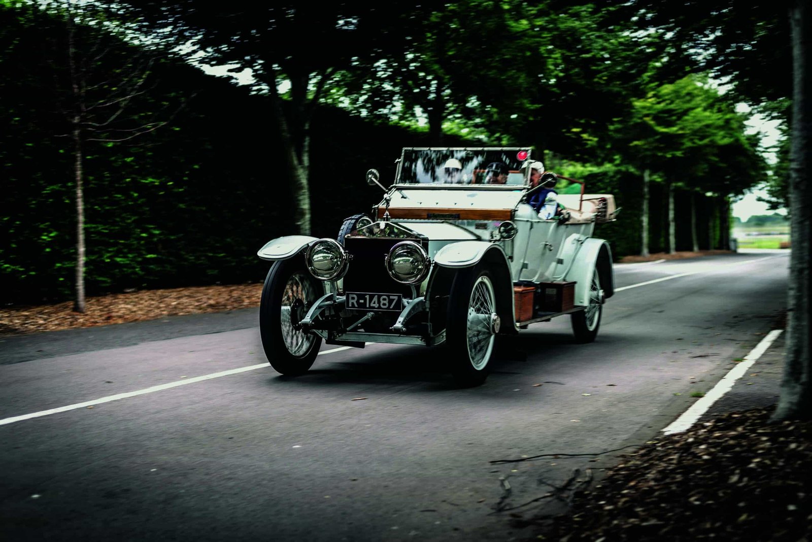 A vintage car is driving down a country road.
