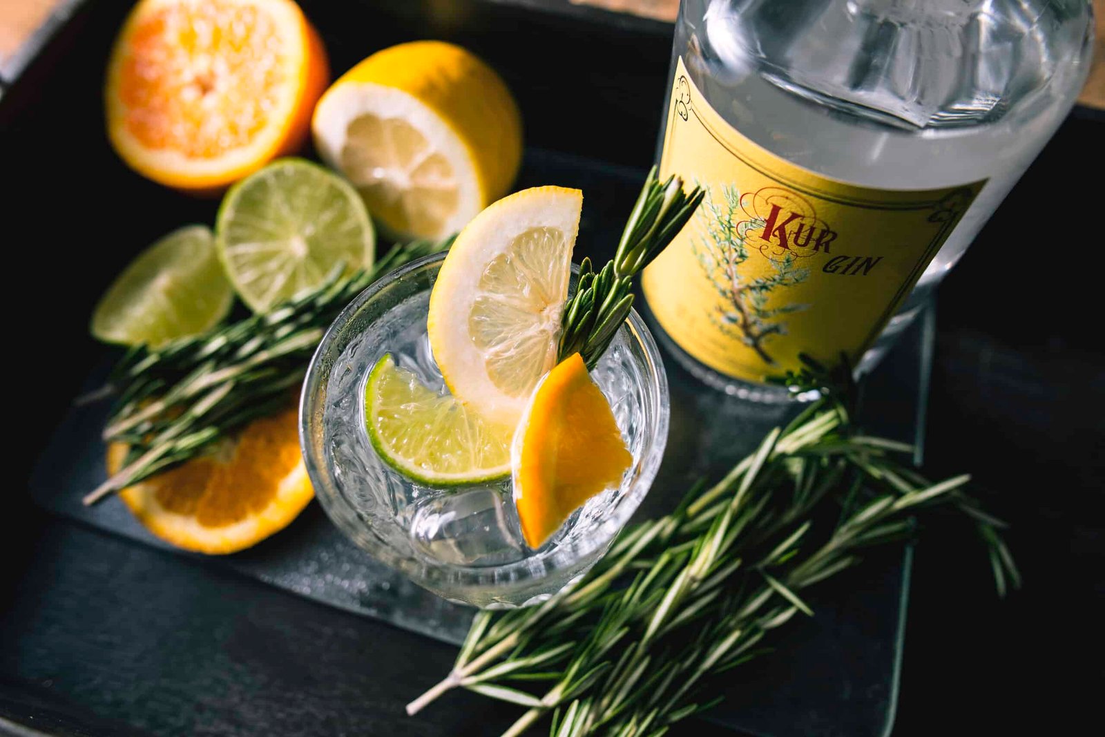 A tray carrying a bottle of natural gin, accompanied by lemons, limes, and a hint of rosemary, embarking on its journey.