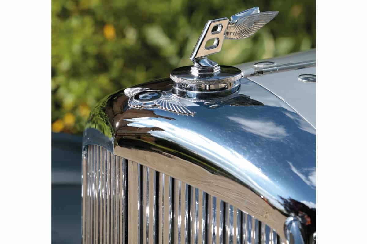 A close up of the hood ornament of both a silver car.