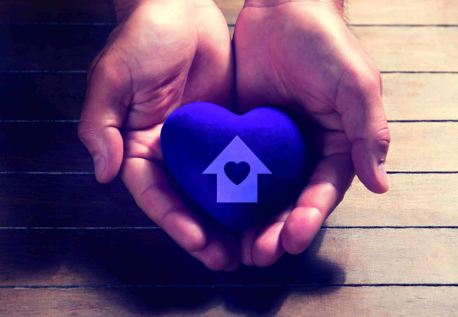 Two hands turning dreams into reality, holding a blue heart with a house on it.