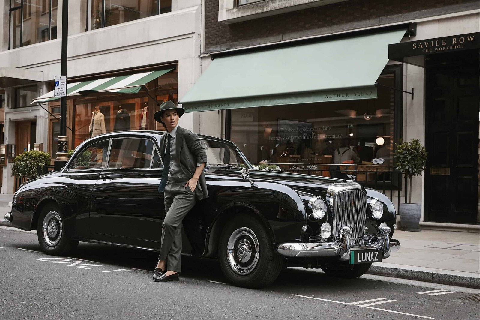 An old man is standing next to a black Bentley car.