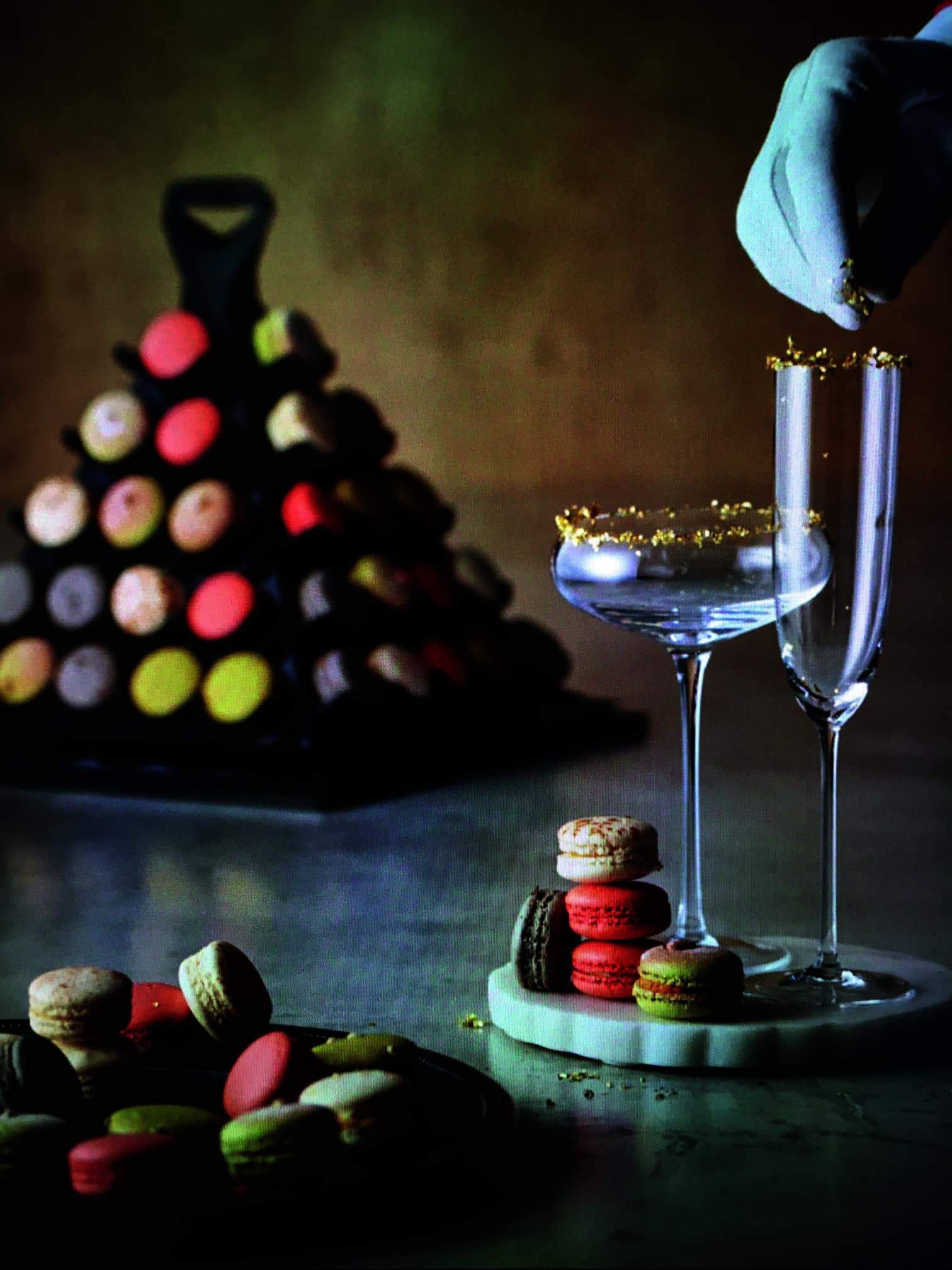A person is pouring a glass of champagne onto a plate of macarons at a classy French event.