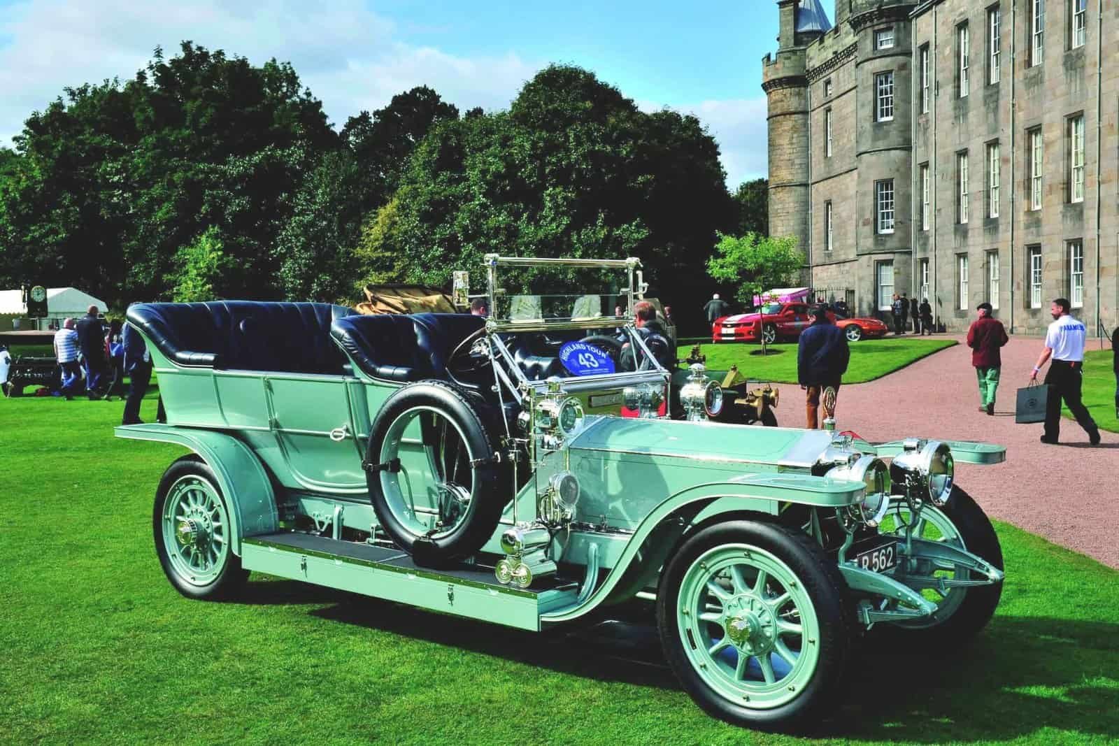 A wind-shaped vintage car is on display in front of a castle.